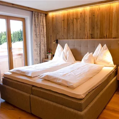 A cozy bedroom with a large double bed and two pillows. The wooden walls and curtains create a warm, inviting atmosphere.