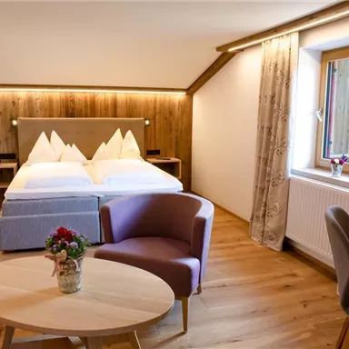 A cozy hotel room with a double bed and a seating area. The wooden paneling creates a warm atmosphere.