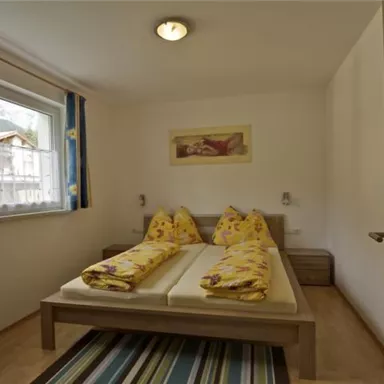 Ein einfaches Schlafzimmer mit einem Doppelbett und gelben Bettdecken. Das Zimmer hat ein Fenster mit Blick nach draußen und einen Holzfußboden.