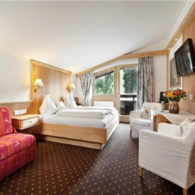 A cozy hotel room with wooden paneling and a large window. There is a double bed, a television, and a seating area.