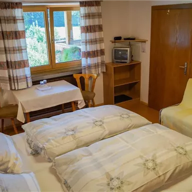 Ein gemütliches Zimmer mit einem Doppelbett, einem Tisch und Stühlen. Das Zimmer hat Fenster mit Blick ins Grüne und eine gemütliche Atmosphäre.