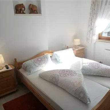A cozy bedroom with a large double bed and decorative pillows. Next to the bed are nightstands with lamps and a window that lets in plenty of light.