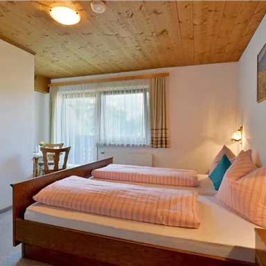 Ein gemütliches Schlafzimmer mit zwei Einzelbetten und einem Holzdecke. Das Zimmer ist hell und freundlich mit einem Fenster und einem Tisch.