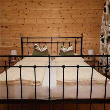 A cozy bedroom with a black iron bed and two pillows. The walls are made of wood, and there are curtains with a floral pattern.