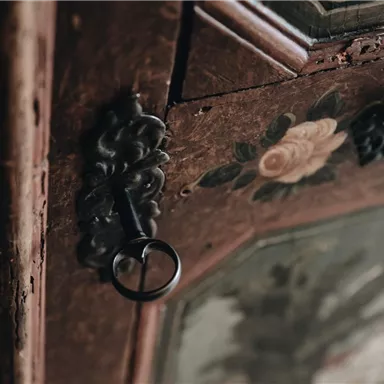 Ein altes Möbelstück mit floralen Verzierungen und einem Schlüssel. Die Holzoberfläche zeigt Patina und Details aus der Vergangenheit.