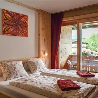 Ein gemütliches Schlafzimmer mit Holzverkleidungen und zwei Betten. Durch das Fenster blickt man auf einen schönen Garten und die umliegende Natur.
