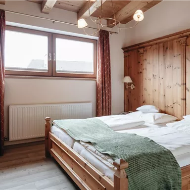 Ein gemütliches Schlafzimmer mit einem Doppelbett und Holzverkleidungen. Große Fenster sorgen für viel Tageslicht und eine warme Atmosphäre.