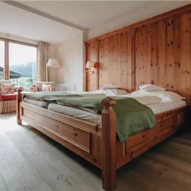 Ein gemütliches Schlafzimmer mit einem großen Holzbett und sanften Textilien. Es gibt einen schönen Ausblick auf die Berge durch die Fenster.