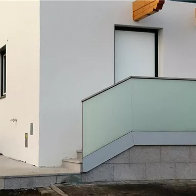 Ein modernes Gebäude mit einer weißen Fassade und einem Zugang mit Geländer. Die Treppe führt zu einem Eingang mit großen Fenstern.