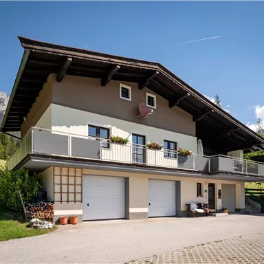 Ein schönes Haus in den Bergen mit einem großen Balkon. Umgeben von Grünflächen und einer klaren blauen Himmel.