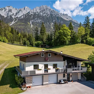 Ein schönes Haus in einer ruhigen Landschaft mit grünen Wiesen und Bergen im Hintergrund. Der Himmel ist klar und die Natur ist üppig.