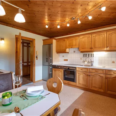 Eine moderne Küche mit Holzschränken und hellen Beleuchtung. Der Tisch ist schön gedeckt und die Atmosphäre ist einladend.