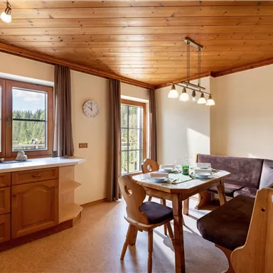 Eine gemütliche Küche mit Holzmöbeln und einem Esstisch. Große Fenster bieten einen Blick auf die Natur.