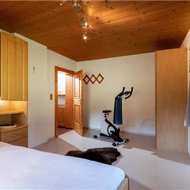 Ein helles Schlafzimmer mit Holzregalen und einem bequemen Bett. Im Raum steht ein Fitnessgerät und es gibt ein Fenster mit Sicht nach draußen.