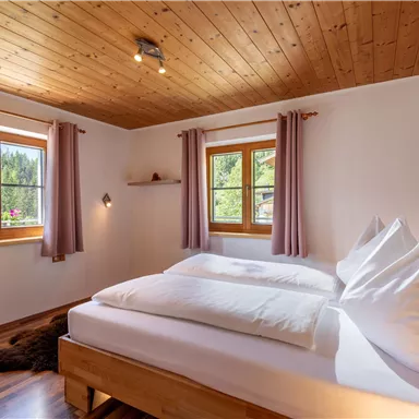 Ein gemütliches Schlafzimmer mit Holzdecke und großen Fenstern. Das Raumdesign ist hell und einladend, mit einem Doppelbett und sanften Vorhängen.