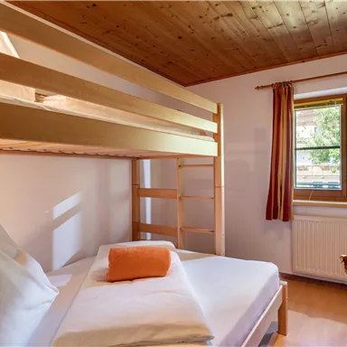 Ein gemütliches Schlafzimmer mit einem Etagenbett und einem Einzelbett. Helle Wände und Holzdetails schaffen eine einladende Atmosphäre.
