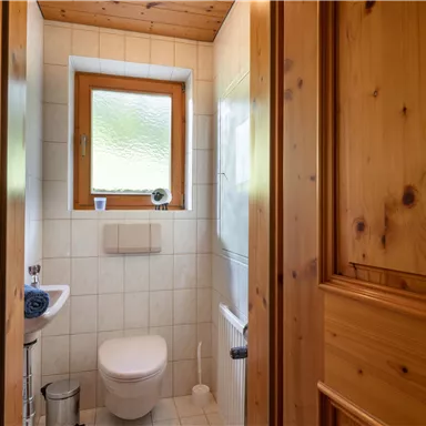 Ein kleines Badezimmer mit Holzvertäfelung. Es gibt eine Toilette, ein kleines Waschbecken und ein Fenster.