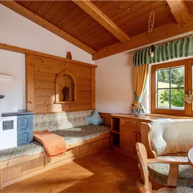 Ein gemütliches Holzinterieur mit einer Sitzecke und einem Esstisch. Große Fenster lassen viel Tageslicht herein und bieten einen Blick ins Grüne.