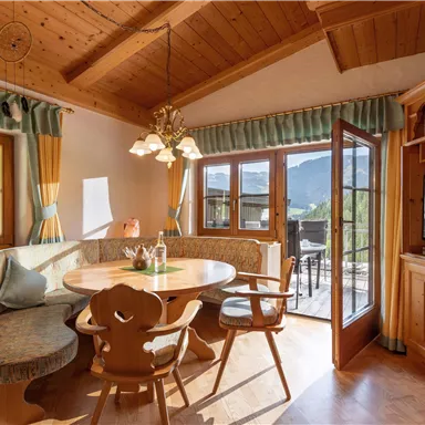 Ein gemütlicher Essbereich mit einem runden Tisch und Holzstühlen. Große Fenster bieten einen Blick auf die Berge und den Außenbereich.