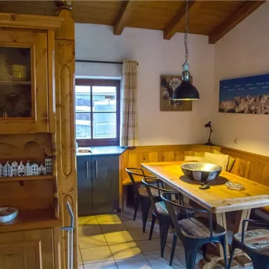 Eine gemütliche Küche mit Holzdetails und einem Esstisch. Die Fenster lassen viel Tageslicht herein.