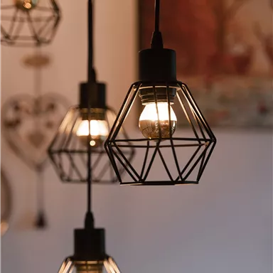 Ein modernes Lampendesign aus schwarzem Metall mit glühenden Glühbirnen. Die Lampen hängen in verschiedenen Höhen und schaffen eine gemütliche Atmosphäre.