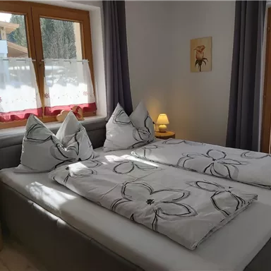 Ein gemütliches Schlafzimmer mit einem Doppelbett und modernen Kissen. Das Zimmer hat große Fenster, die für viel Tageslicht sorgen.