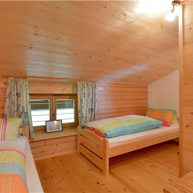 Ein gemütliches Schlafzimmer mit Holzwänden und zwei Einzelbetten. Große Fenster sorgen für viel Tageslicht.