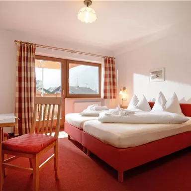 Ein gemütliches Hotelzimmer mit zwei Betten und einem Tisch. Große Fenster sorgen für viel Tageslicht.