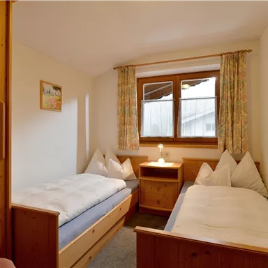 Ein gemütliches Schlafzimmer mit zwei Einzelbetten und einem Nachttisch. Große Fenster erlauben viel Tageslicht und eine angenehme Atmosphäre.
