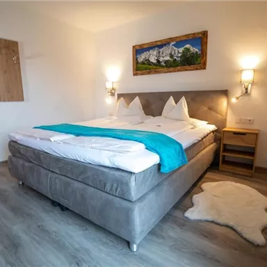 Ein gemütliches Schlafzimmer mit einem großen Bett und hellen Wänden. Ein stilvolles Gemälde und sanfte Beleuchtung schaffen eine entspannte Atmosphäre.