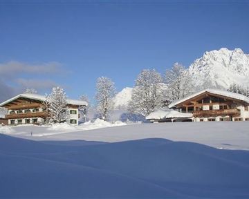 Eine schöne winterliche Landschaft mit schneebedeckten Hütten und hohen Bergen im Hintergrund. Der klare blaue Himmel vervollständigt die idyllische Szene.