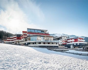 Ein modernes Hotelgebäude in einer schneebedeckten Landschaft. Im Hintergrund sind Berge und ein klarer blauer Himmel sichtbar.