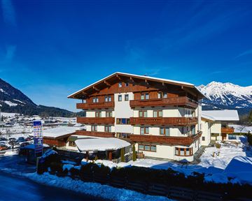 A charming building in Alpine style surrounded by snow and mountains. The sky is clear and blue, creating an inviting atmosphere.