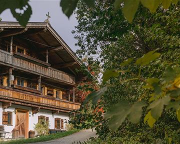 A traditional wooden house with multiple floors and a green garden. Surrounded by trees and a peaceful landscape.