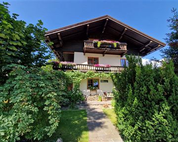 Ein schönes Alpenhaus mit einem großen Balkon und blühenden Pflanzen. Der Garten ist grün, gut gepflegt und lädt zum Verweilen ein.