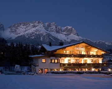 Ein schönes, beleuchtetes Gebäude im Schnee bei Nacht. Im Hintergrund erheben sich majestätische Berge.