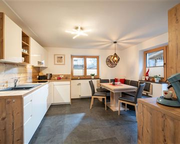 Eine moderne Küche mit Holz- und Weißtönen. Es gibt einen Essbereich mit einem Tisch und Stühlen sowie ausreichend Tageslicht.