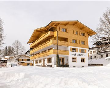 A pretty wooden building in winter with a snow-covered ground. The name "Auhof" is clearly visible.