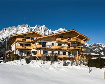 A modern chalet in the snow with a view of the mountains. The clear blue sky complements the winter landscape.