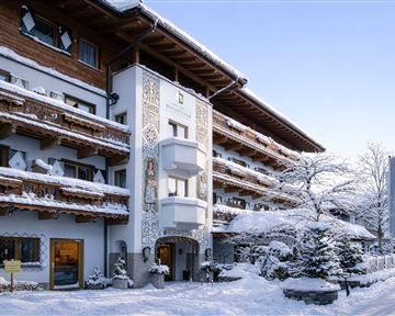 A charming hotel in winter with snow-covered balconies and decorative details. The surroundings are calm and idyllic, perfect for a relaxing stay.