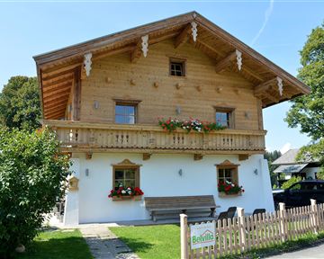 A traditional wooden-clad house with a balcony and colorful flowers. The sunny day gives the scene an inviting atmosphere.