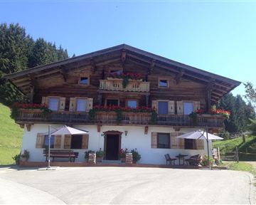 Ein traditionelles Holzhaus mit Balkonen voller Blumen. Es befindet sich in einer malerischen ländlichen Umgebung mit grünen Hügeln.