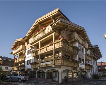 Ein charmantes Gebäude im alpinen Stil mit mehreren Balkonen und Blumen. Die klare Sicht auf die Berge im Hintergrund ergänzt die malerische Kulisse.