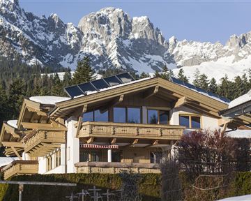 A modern chalet in the mountains with snow-covered peaks in the background. The architecture combines wood and large windows that bring in plenty of light.