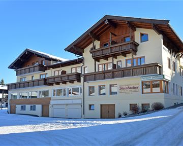 Ein modernes Gebäude mit mehreren Etagen und Balkonen, umgeben von Schnee. Der klare Himmel ergänzt die winterliche Landschaft.