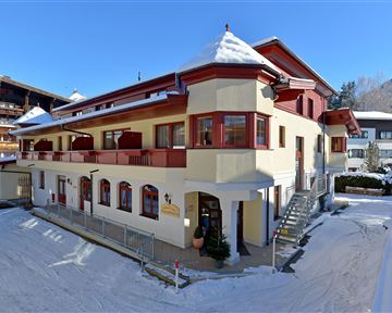 A charming building in winter with snow on the roof. Surrounded by snowy hills and blue sky.