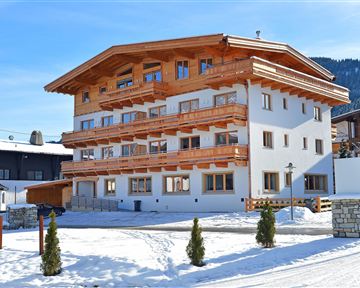 Ein modernes Gebäude im alpinen Stil, umgeben von Schnee. Die Fassade besteht aus Holz und ist hell gestrichen.