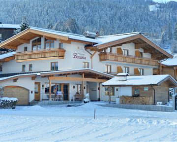 Ein gemütliches Holzhaus im winterlichen Schnee. Die Umgebung ist von verschneiten Bäumen und Bergen umgeben.