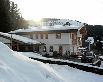 Ein charmantes Chalet im Schnee mit Bergen im Hintergrund. Die Sonne scheint sanft auf das Gebäude und die Umgebung.