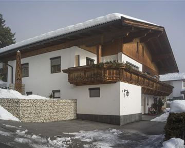Ein gemütliches Chalet im Schnee mit einem traditionellen Balkon aus Holz. Die Umgebung ist winterlich und friedlich.